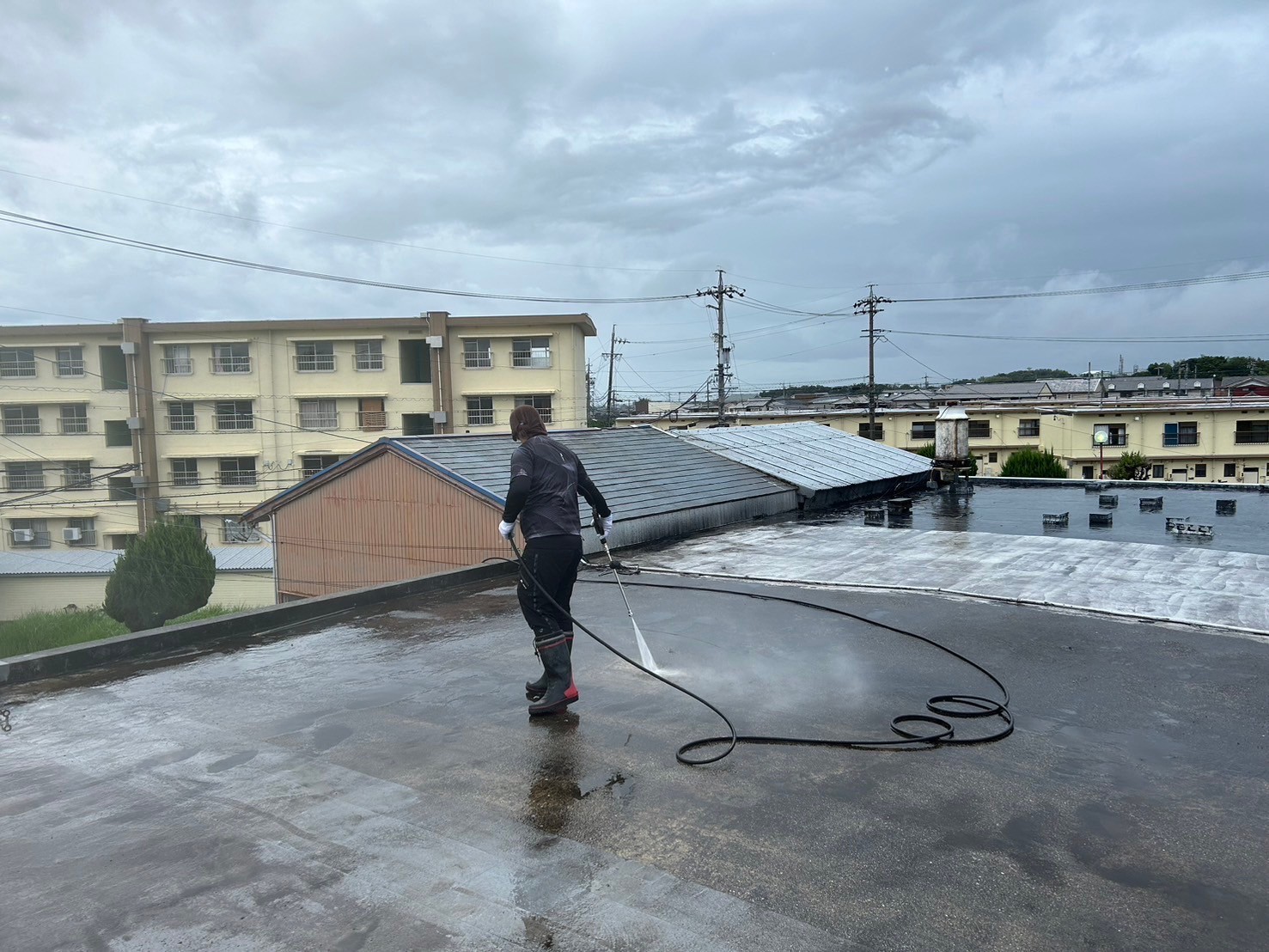 桑名市の長屋住宅のコンクリート陸屋根、ウレタン防水工事で高圧洗浄機を使用して下地の汚れを洗い流している所